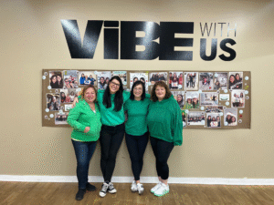 Four SIMPLE Coaching members wearing green shirts standing together under a “Vibe With Us” sign during a weight loss group session.