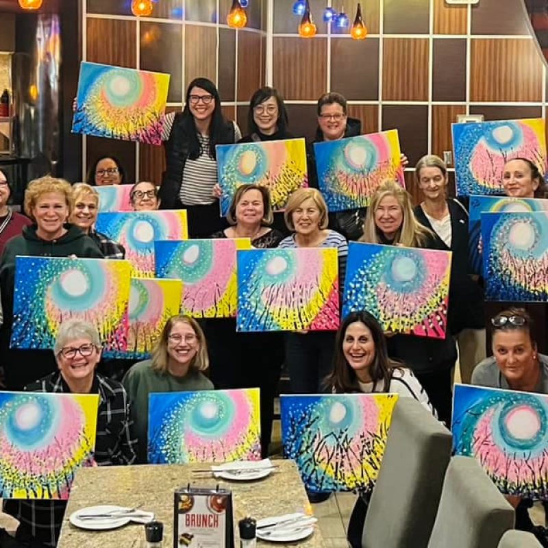 Members at SIMPLE Coaching weight loss group meetings holding colourful paintings together in a community event